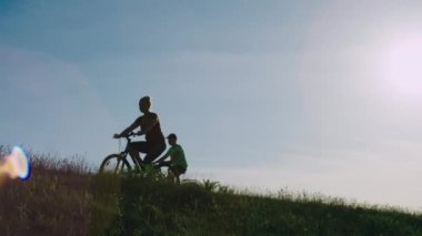 Aile gün batımında doğada bisiklete biner. Anne ve oğul yaz güneşinde bir tarlada bisiklet sürerler..