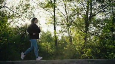 Parkta koşan bir kadın. Kız gün batımında yolda koşar. Doğada ağaçlarla. Aktif eğlence yaşam tarzı ve spor.