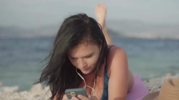 해변에 누워서 헤드폰으로 음악을 방식의 수영복을 옆에서 전화로 음악을 긴장을 — 비디오