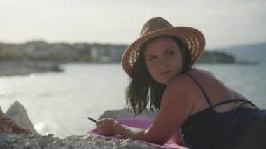 Telefonu olan kız deniz kenarında güneşleniyor. Güzel muhabir kadın gün batımında deniz kenarında kumsalda yemek sipariş ediyor..