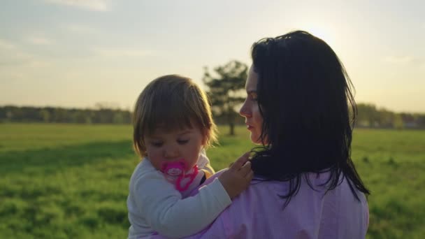 日落时 妈妈抱着一个小女孩在自然景观中 快乐在一起 温柔和父母的爱 阳光的光芒 — 图库视频影像