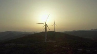 Gün batımında elektrik üreten yel değirmenlerinin hava manzaralı silueti. Güzel bir manzarada dağlardaki rüzgar enerjisinden gelen temiz ve ekolojik elektrik..