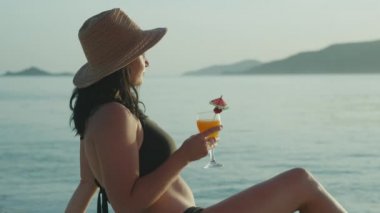 Deniz kenarında elinde kokteyl bardaklarıyla dinlenen bir kız. Okyanusun kenarında meyve suyu içen mutlu bir kadın..