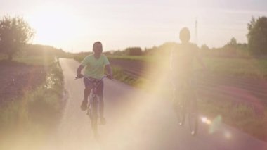 Aile yazları açık hava aktiviteleri, anne ve oğlu bisiklete biniyor. Günbatımında parkta bisiklet süren kadın ve çocuk..