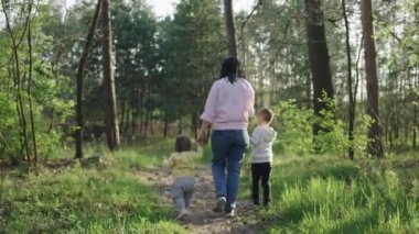 Çocuklu anne ormanda yürüyor, aile birlikte mutlu. Kadın ve erkek parkta yolda yürüyor.
