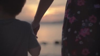 Anne gün batımında oğullarını deniz kenarında tutuyor. Birlikte tatilde okyanus kıyısında mutlu bir aile..