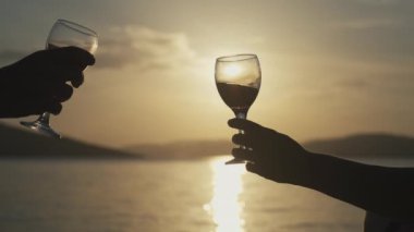 Deniz kenarındaki mutlu çift şarap kadehlerini deviriyor. Romantik bir randevuda, güzel bir manzarada tezahürat kadehlerinin yakın çekimi..