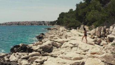 Hava manzaralı kız kayalıklarda yürür ve deniz manzaralı bir yerde uzanır. Okyanus kıyısında tatil yapan kadınlar güneşte neşelenir ve dinlenir..