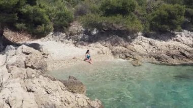 Deniz kenarında tek başına mayo giymiş hava manzaralı kız. Güzel bir kadın okyanus kıyısında güzel bir kaya ve dağ manzarasında tatil yapıyor..