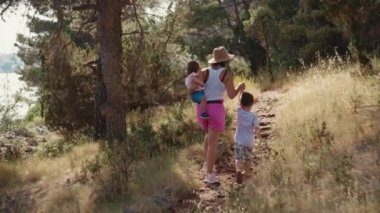 Mutlu bir aile doğa yürüyüşünde ağaçların ve çimenlerin yanında. Güzel bir manzara ve annesi ile oğlu ve kızı birlikte yolda yürüyorlar..
