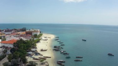 Hava manzaralı Zanzibar Tanzanya. Eski evleri ve sokakları kumlu bir plajla teknelerin durduğu Hint Okyanusu ile ayıran kıyı şeridi üzerinde bir dron uçuyor. Güzel peyzaj drone videosu.