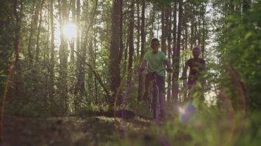 Anne ve oğlu gün batımında ormanda yürüyüşe çıktılar. Kadın ve çocuk güzel manzaralı, aktif yaşam tarzı ve dinlenme yerlerinde off-road bisikleti sürüyorlar..