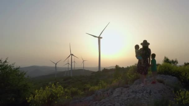 日没時に風車の近くの山の中で空中ビューの家族のお母さんと子供たち 人々ときれいな風力エネルギーの生産は 美しい風景の中に旅行 — ストック動画