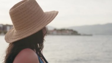 Şapkalı mutlu beyaz kız denize ve dalgalara bakıyor. Okyanus kenarında tatil yapan bir kadın gün batımında dinlenir..