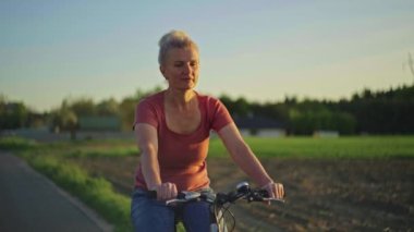 50 yaşında bir kadın parkta bisiklete biniyor. Spor yapan mutlu yaşlı bir adamın ve bisiklet süren aktif bir yaşam tarzının yavaş çekim videosu..