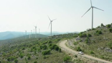 Dağlardaki yel değirmenlerinin ve araba seyahatlerinin havadan görüntüsü. Doğa manzarası ve havadan, insanlardan ve doğadan temiz bir enerji kaynağı.