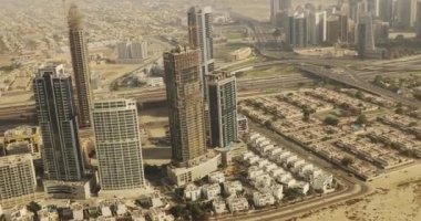 Hava manzaralı Dubai. İnşaat halindeki gökdelenlerin üzerinden uçuyor. Çölde yer alan bir şehirde şehrin cam binaları ve cadde kavşakları olan vinçler var..