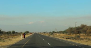 Yerlilerin asfalt yolda nasıl yürüdüğünü görebileceğiniz Afrika 'daki bir yolun görüntüsü. Arka planda büyük bir dağ görebilirsin Kilimanjaro..