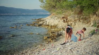 Anne ve oğlu sahili çöpten temizliyor. Aile güzel bir manzarada balonların içinde çöp toplar. Karanın ve okyanusun ve ekolojinin korunması.