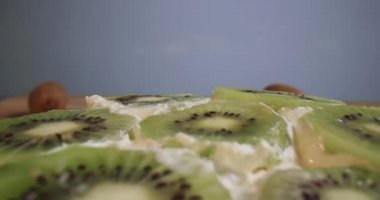 Sağlıklı yemek tatlı kivi keki. Doğum gününde mutfakta yoğurt ve meyve çevirmeleriyle süslenmiş taze, tatlı bir pasta. Yavaş çekim 4K vejetaryen yemeği videosu.