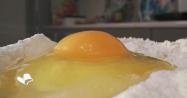 自家製生地を作る 卵黄と卵の白い手は 台所のテーブルの上にケーキやパンを焼くための白い小麦粉に壊れます4Kタイムラプスビデオ — ストック動画