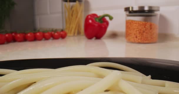 新鮮な天然パスタを調理します キッチンで調理されたスパゲッティは プレート上にあり パルメザンチーズを振りかけ 背景には野菜 チェリートマト ピーマンがあります 4K遅いビデオ — ストック動画