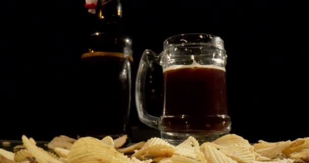酗酒者喝深色啤酒 桌上有一个瓶子 薯片和一杯含有气泡和泡沫的黑啤酒 在酒吧或酒吧里为派对喝一杯 4K慢动作视频 — 图库视频影像