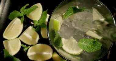 Ferahlatıcı bir yaz içkisi mojito ya da limonata hazırlıyorum. Limon, nane ve buz, soğuk bir içecek için içine karbonatlı su eklenen bir bardakta bulunur. 4K yavaş çekim videosu.