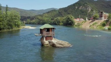 Hava saldırısı Sırbistan 'ı vurdu. Nehrin ortasında kayaları, suyu, ormanı ve ağaçları ve manzarayı, güzel dağları görebileceğiniz bir kayanın üzerinde duran insansız hava aracı videosu..