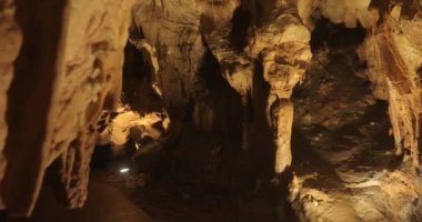 Potpecka Mağarası Sırbistan. Taş ve kayalarla aydınlatılmış dar tünelleri olan bir mağaradaki dikitler ve sarkıtlardan güzel buz sarkıtları dengeleyicisinin videosu..