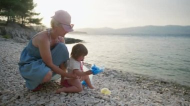 Anne ve kızı sahili çöpten temizliyor. Çocuk plajdaki çöpe plastik atıyor..