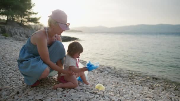 母親と娘はゴミからビーチをきれいにした 子供は海岸のゴミの中にプラスチックを投げます — ストック動画