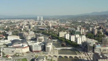 Üsküp Makedonya havacılık manzarası. Şehir merkezinde gemileri, köprüleri, evleri, gökdelenleri, sokakları, arka planda dağları olan bir insansız hava aracı Vardar nehrinin üzerinden uçtu..