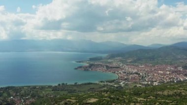 İnsansız hava aracı, tepeler, kayalar ve manzarayla dağların üzerinden uçarak Ohri Gölü 'ne tepeden bakan güneş ışınları ve evleri ve caddeleriyle kentin üzerinden geçiyor. Makedonya 'nın hava görüntüsü.