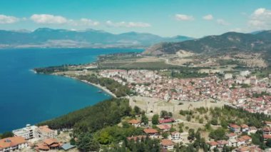 Hava saldırısı Ohri Makedonya 'yı vurdu. Kırmızı çatıları ve güzel manzarası olan evleri olan bir şehirle çevrili bir dağın tepesinde duran kuleleri olan bir kalenin insansız hava aracı videosu. Yüksek kalite 4k görüntü