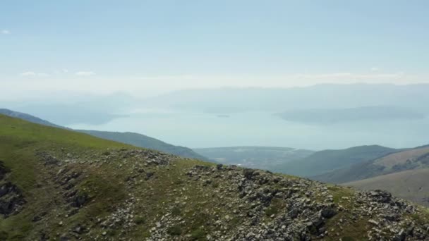 手前の山脈とその背後にある村と湖が岩や木のピークに囲まれているオリード湖のドローンビデオ 空中展望マケドニア 高品質4K映像 — ストック動画