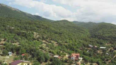 Orman ve tepeleri olan dağlarda evleri ve kırmızı çatıları olan bir köyün insansız hava aracı videosu. Makedonya 'yı hava saldırısı vurdu. Yüksek kalite 4k görüntü