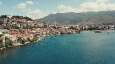 Dağın tepesinde kırmızı çatıları olan güzel manzaralı bir gölün kıyısında duran bir şehrin insansız hava aracı videosu. Hava manzaralı Ohri Makedonya. Yüksek kalite 4k görüntü