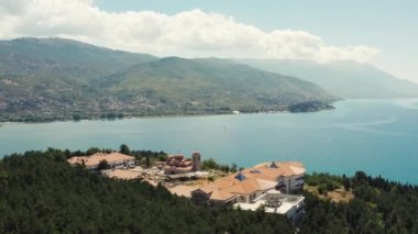Ohri Makedonya 'nın havadan görünüşü. Dağın tepesinde kırmızı çatılı bir kilisenin insansız hava aracı videosu. Arka planda bir göl ve Ohri şehri. Sokakları, evleri, tekneleri ve güzel manzarası olan..