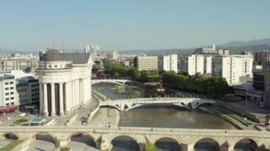 Üsküp Makedonya havacılık manzarası. Şehir merkezinde gemileri, köprüleri, evleri, gökdelenleri, sokakları, arka planda dağları olan bir insansız hava aracı Vardar nehrinin üzerinden uçtu.. 