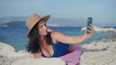 Kız sahilde çitleri aşıyor ve telefonda selfie çekiyor. Tatilde güzel bir kadın okyanusun anısına fotoğraf çekiyor..