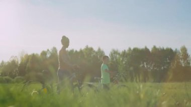 Anne ve oğlu gün batımında bisikletle tarlaya gidiyorlar. Aile, parkta aktif olarak birlikte zaman geçirir. Mutlu anne ve bebek birlikte. Yüksek kalite 4k görüntü