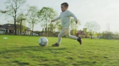 Çimlerin üzerinde oynayan çocukların çocukluk yavaş çekim videosu. Üç çocuk birlikte aktif bir oyun oynayarak topa vuruyor, futbol insanları birleştiriyor..