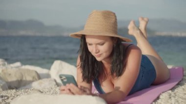 Kız sahilde deniz kenarında oynayacak ve telefonla yazışacak. Okyanustaki güzel kadın ve dağ manzarası alete bir mesaj yazar..