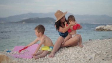 Anne ve çocuklar sahilde oyuncaklarla oynuyorlar. Güzel okyanus manzarası ve ailesi tatilde birlikte mutlu ve gülümsüyor..