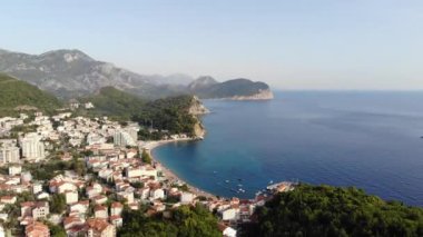 Karadağ 'daki Adriyatik Denizi kıyısındaki Petrovac kasabası. Arka planda dağ manzarası ve marinası olan koyu kırmızı fayanslı evler olan bir kasaba. Yüksek kalite 4k görüntü