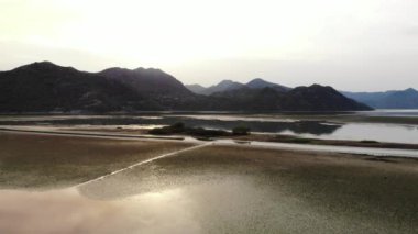 Havadan Skadar Gölü Karadağ 'ı çektiler. Gün batımında dağlarda çimenli bir gölün drone videosu. Dağ manzarası, kayalar, su ve yeşillik. Yüksek kalite 4k görüntü