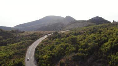 Karadağ havadan görünüyor. Adriyatik Denizi 'nin arka planında, dağların arasından geçen arabaların, kayalıklarda ağaçların olduğu bir yolun insansız hava aracı videosu. Güzel manzaralı dağların tepeleri.