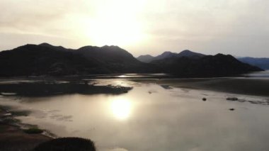 Havadan Skadar Gölü Karadağ 'ı çektiler. Gün batımında dağlarda çimenli bir gölün drone videosu. Dağ manzarası, kayalar, su ve yeşillik. Yüksek kalite 4k görüntü