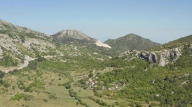 Ormanlar, dağlar, zirveler ve güzel manzaralı tepelerle çevrili ovalarda evleri olan bir köyün insansız hava aracı videosu. Karadağ 'dan hava görüntüsü. Yüksek kalite 4k görüntü